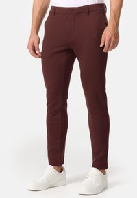 Burgunderfarbene Tailor-Hosen mit schmaler Passform, seitlichen Taschen und Knopfverschluss, kombiniert mit weißen Sneakern. Glattes, dehnbares Material.