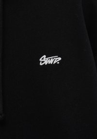 Tissu noir avec texte stylisé brodé en blanc "Swir." centré, montrant une partie d'un sweat à capuche avec cordon sur le côté gauche.
