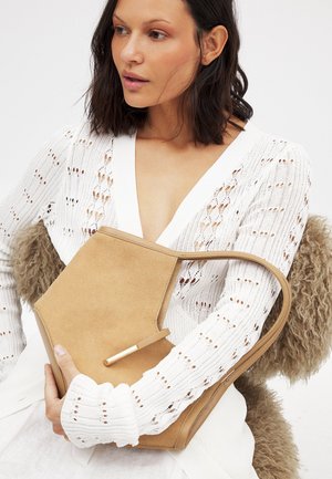Beige suède handtas met een unieke hoekige vorm, met een gouden accent op het handvat. Draagt men met een witte gebreide trui.