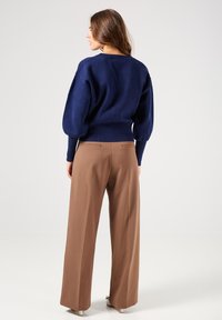 Suéter de punto azul marino con mangas abullonadas, combinado con pantalones marrones de pierna ancha y cintura alta que cuentan con dos bolsillos traseros y una textura suave.