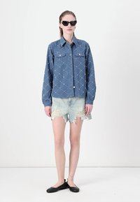 Jeansjakke med diamanter og nagler, lyseblå distressed shortser og svarte leiligheter. Modellen bruker svarte solbriller, håret trukket tilbake.