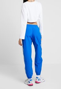 Top blanco de manga larga recortada combinado con pantalones deportivos azules brillantes con franjas laterales. Llevado con zapatillas deportivas blancas y rosas.