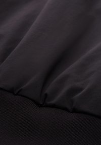 Gros plan sur un tissu noir avec des coutures froncées au-dessus d'un bord-côtes côtelé, mettant en valeur le contraste de texture et de matériau.