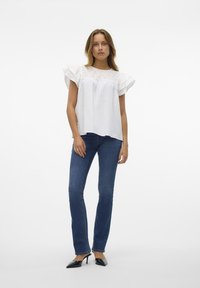Vit kortärmad blus med volangärmar, prydd med broderade detaljer vid oket. Matchas med mörkblå slim-fit jeans och svarta klackar.