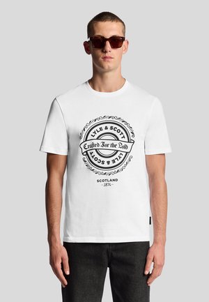Witte katoenen t-shirt met korte mouwen met een zwart, cirkelvormig logo in het midden dat "LYLE & SCOTT" zegt en "Gemaakt voor de Dapperen."