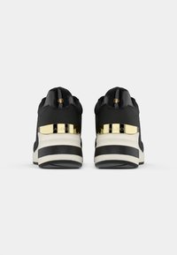 Pair of black sneakers with white and black striped soles, featuring gold metallic detail and logo on the heel.