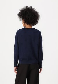 Mørkeblå genser med strukturmønster, rund hals og ribbestrikkede mansjetter. Stoffet ser mykt og lett ut, vist fra baksiden.