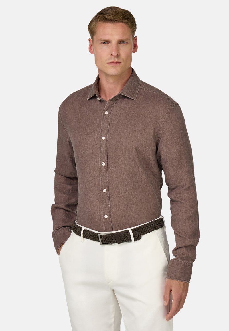 Camicia a maniche lunghe marrone con un motivo testurizzato, colletto alla francese e bottoni bianchi, indossata con una cintura intrecciata marrone e pantaloni bianchi.