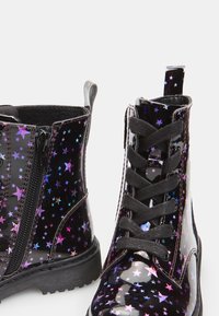 Botas de charol negro con patrones de estrellas en púrpura y azul. Cuentan con un zip lateral, cordones y suelas de goma texturizadas.