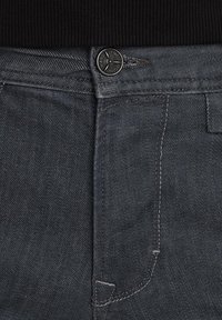 Dunkelgraue Denim-Jeans mit einem Metallknopf am Bund, kontrastierender Naht und einer glatten Textur mit einem leichten Glanz.