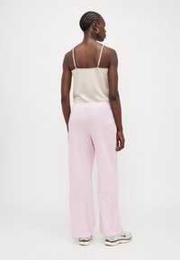 Lyserosa linbukse med vide ben og elastisk liv, kombinert med en beige satengcamisole, som viser en jevn tekstur og avslappet passform.