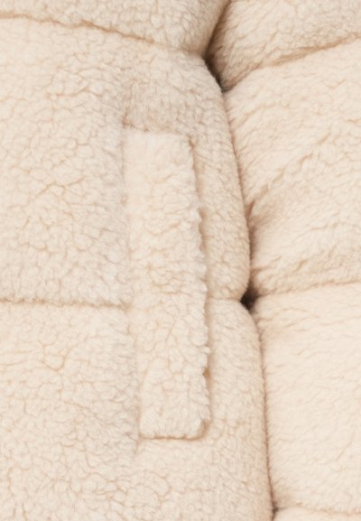 Beige fluffy fleece fabric with a soft, textured surface; features a visible seam and a small rectangular pocket on the side.