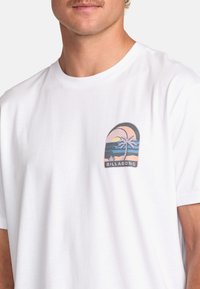 White short-sleeve t-shirt with a colorful palm tree graphic and beach scene printed on the left chest area. Soft cotton material.
