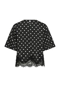 Blouse noire à manches courtes avec des pois blancs. Présente une bordure en dentelle à l'ourlet et une fermeture par bouton au dos. Texture lisse.