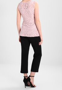 Ljusrosa spets utan ärmar med en åtsittande design, kombinerad med svarta kaprinbyxor och svarta klacksandaler. Slät textur och intrikat mönster.