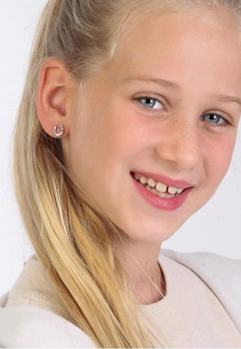 Silberne Hufeisenohrringe mit kleinen funkelnden Akzenten, die an einem hellhäutigen Mädchen mit langen blonden Haaren befestigt sind und lächelt.