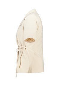 Haut à manches courtes beige en wrap, avec un col et un détail noué à la taille, fabriqué dans un tissu à texture lisse.
