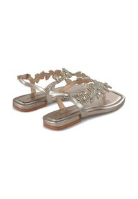 Sandali metallici argento presentano un motivo decorativo a foglia con dettagli in strass, suola piatta e chiusura a fibbia. Texture liscia e design aperto.