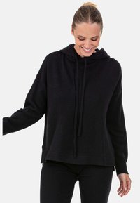 Sweat à capuche noir en matière douce avec une coupe décontractée, poignets côtelés et cordon à la base du cou. Texture lisse et design minimaliste.