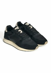 Zapatillas negras que combinan ante y malla, con punta redonda, cordones y una suela de goma de color claro. Incluyen detalles como un talón beige.