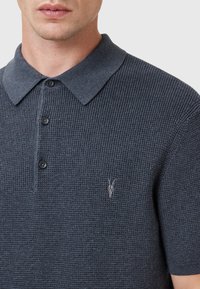 Koszulka polo z krótkim rękawem w ciemnoszarym, teksturowanym materiale. Posiada kołnierzyk, zapięcie na trzy guziki oraz naszywkę z logo na piersi.