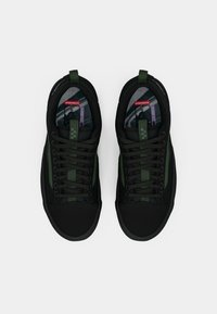 Crne tenisice s ljubičastim bočnim prugama, teksturiranom tkaninom, okruglim vrhom i dizajnom s vezanjem. Uključuju uzorčanu unutarnju podstavu i petlju za povlačenje.