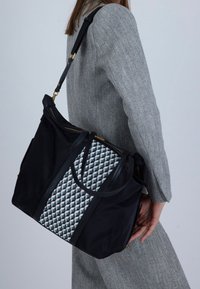 Zwarte stoffen draagtas met een geometrisch grijs-wit motief, voorzien van dubbele bovenhandvatten en een ritssluiting, afgewerkt met gouden beslag.