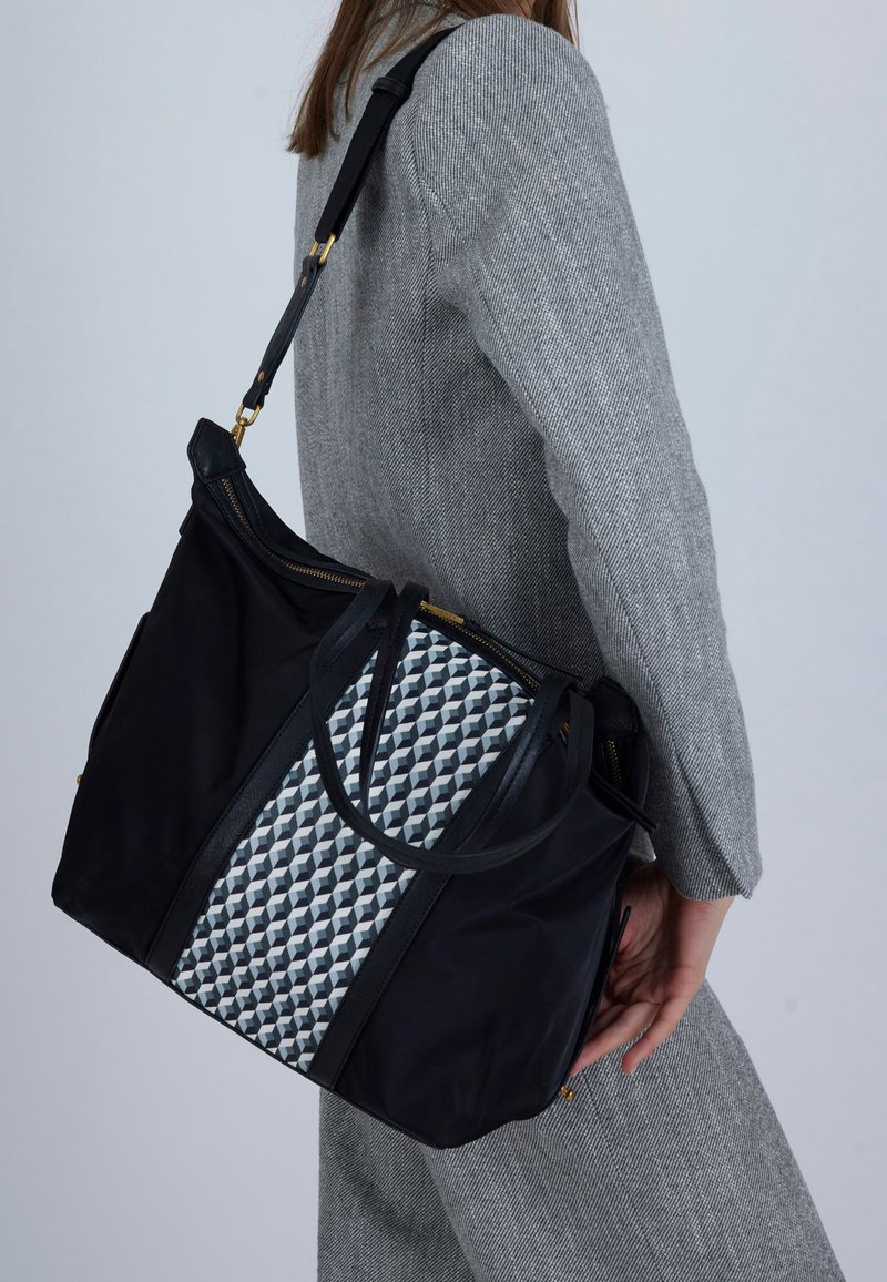 Zwarte stoffen draagtas met een geometrisch grijs-wit motief, voorzien van dubbele bovenhandvatten en een ritssluiting, afgewerkt met gouden beslag.