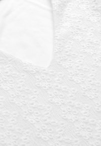 Vit tyg med en texturerad blommönster, med en djup V-ringning. Materialet verkar mjukt och lätt, vilket betonar de delikata detaljerna.