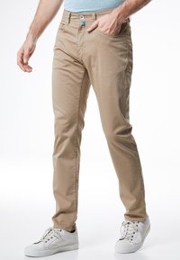 Beige chinos suoran istuvuuden kanssa, joissa on tasainen etuosa, kaksi sivutaskua ja pieni sininen korostuspainike, yhdistettynä valkoisiin lenkkareihin.