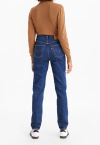 Jeans de mezclilla azul de talle alto con un corte recto, que cuentan con bolsillos traseros y una etiqueta de cuero marrón en la cinturilla.