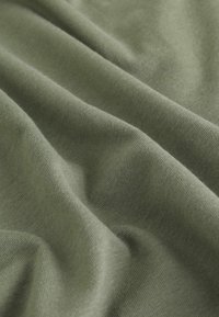 Olivgrüner Stoff mit einer glatten, weichen Textur, der sanfte Falten zeigt und ein leichtes, gestricktes Design aufweist.