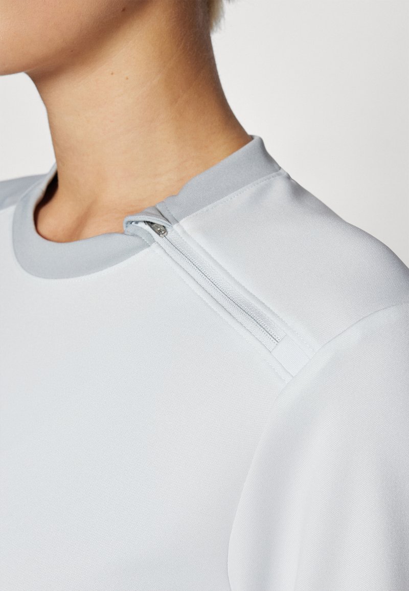 Lichtgrijze sporttop met een gladde stof, ronde halslijn en een ritsdetail aan de schouder voor een verstelbare pasvorm.