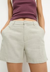 Jasnoszare lniane szorty z przednimi kieszeniami, o luźnym kroju i gładkim pasie. Tkanina ma lekko teksturowany wygląd.