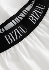 Biały materiał z marszczoną fakturą i czarnym elastycznym pasem z nazwą marki "BIZZUU" w białych literach.