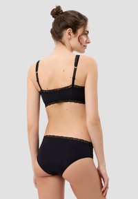 Schwarzes Wäsche-Set bestehend aus einem Bralette mit verstellbaren Trägern und Spitzenbesatz, kombiniert mit passenden hochgeschnittenen Slips, glatte Textur.