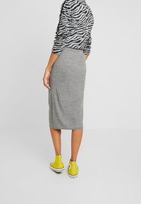 Jupe midi grise à rayures avec une silhouette ajustée et une fente sur le côté, associée à des baskets montantes jaunes vives. Pull à motif zèbre noir et gris.