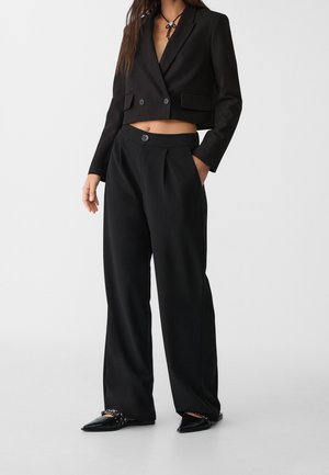 Blazer noir court avec deux boutons, associé à un pantalon large noir soigneusement taillé. Tissu lisse avec un design minimaliste et deux poches.
