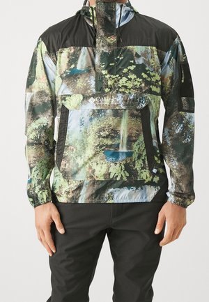Veste à capuche pour homme avec un imprimé nature multicolore représentant une cascade et du feuillage, associée à un pantalon noir.