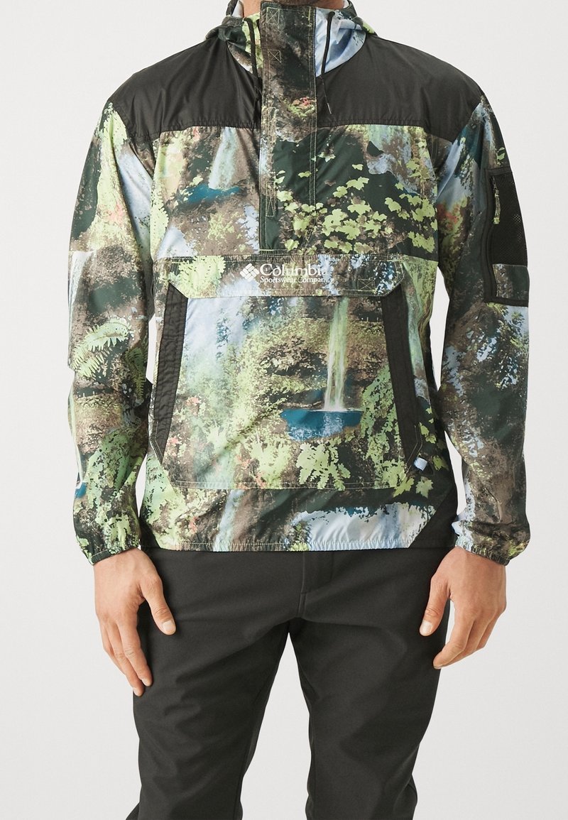 Veste à capuche pour homme avec un imprimé nature multicolore représentant une cascade et du feuillage, associée à un pantalon noir.