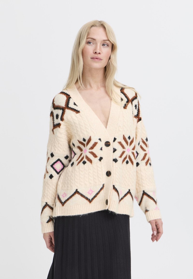 Cárdigan crema con patrones geométricos en marrón, rosa y negro; presenta un escote en V, cinco botones y un punto texturizado.