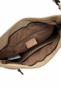 Interno di una borsa a tracolla in pelle beige con rivestimento in tessuto marrone, una tasca con zip, due scomparti aperti e un'etichetta. Texture morbida, chiusura con zip.