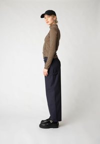 Maglioncino a righe marrone e beige, abbinato a pantaloni larghi blu e scarpe piattaforme nere. Un berretto nero valorizza lo stile casual.