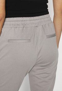 Calças de jogger cinza claro com uma cintura elástica, apresentando dois bolsos traseiros com bordas lisas e uma textura de tecido suave.