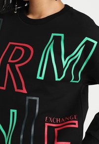 Černá mikina s kapucí s velkými, vícebarevnými písmeny v červené, zelené a modré barvě. Design obsahuje nápis „EXCHANGE“ a volný střih.