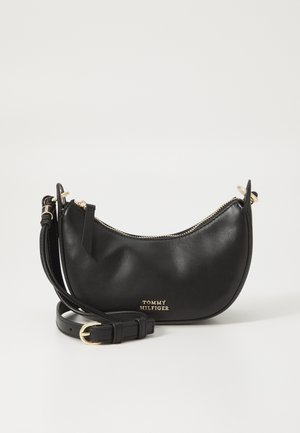 Černá kožená crossbody taška ve tvaru půlměsíce se zlatým zipem, nastavitelným popruhem a logem „Tommy Hilfiger“ ve zlatém provedení.