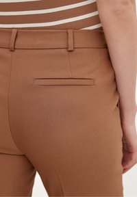 Pantalon marron sur mesure avec une texture lisse, doté d'une poche arrière et d'une ceinture. Le tissu présente un léger éclat.