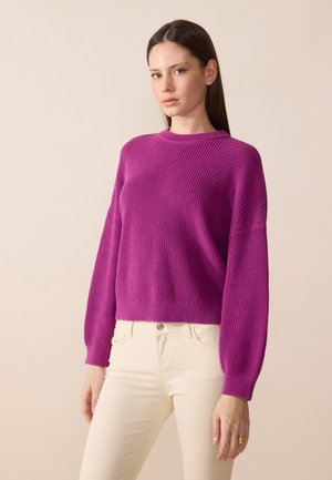 Magenta ribbed knit sweater with a crew neck and wide sleeves, paired with light-colored fitted pants. Smooth texture, cropped design.
