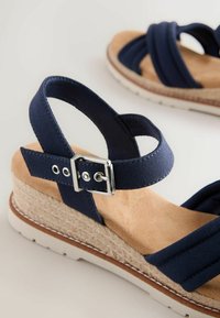 Sandales compensées bleu marine avec brides à boucle réglables, semelle intérieure beige rembourrée, semelle intermédiaire en jute tressée et semelle extérieure en caoutchouc blanc.