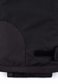 Chaqueta aislante negra con textura suave, que presenta acentos redondeados en los hombros y un fondo elástico. Incluye un detalle de cierre de Velcro.